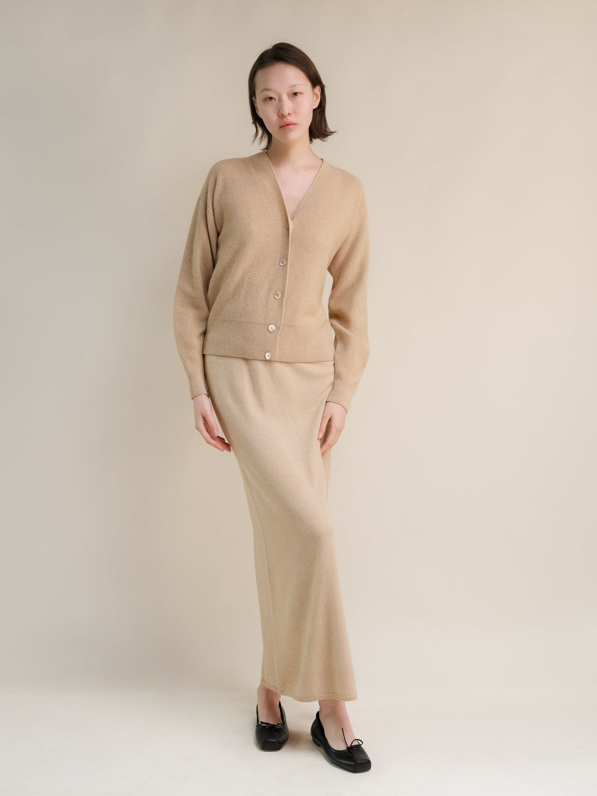 Beige cashmere blend cardigan with a matching high waist long knit skirt worn by a model.