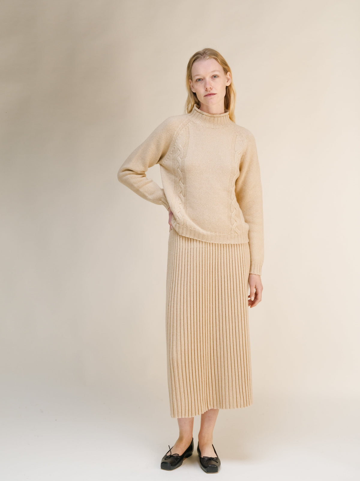 Modelo con a beige jersey de punto trenzado and falda midi acanalada a juego against a neutral backdrop.