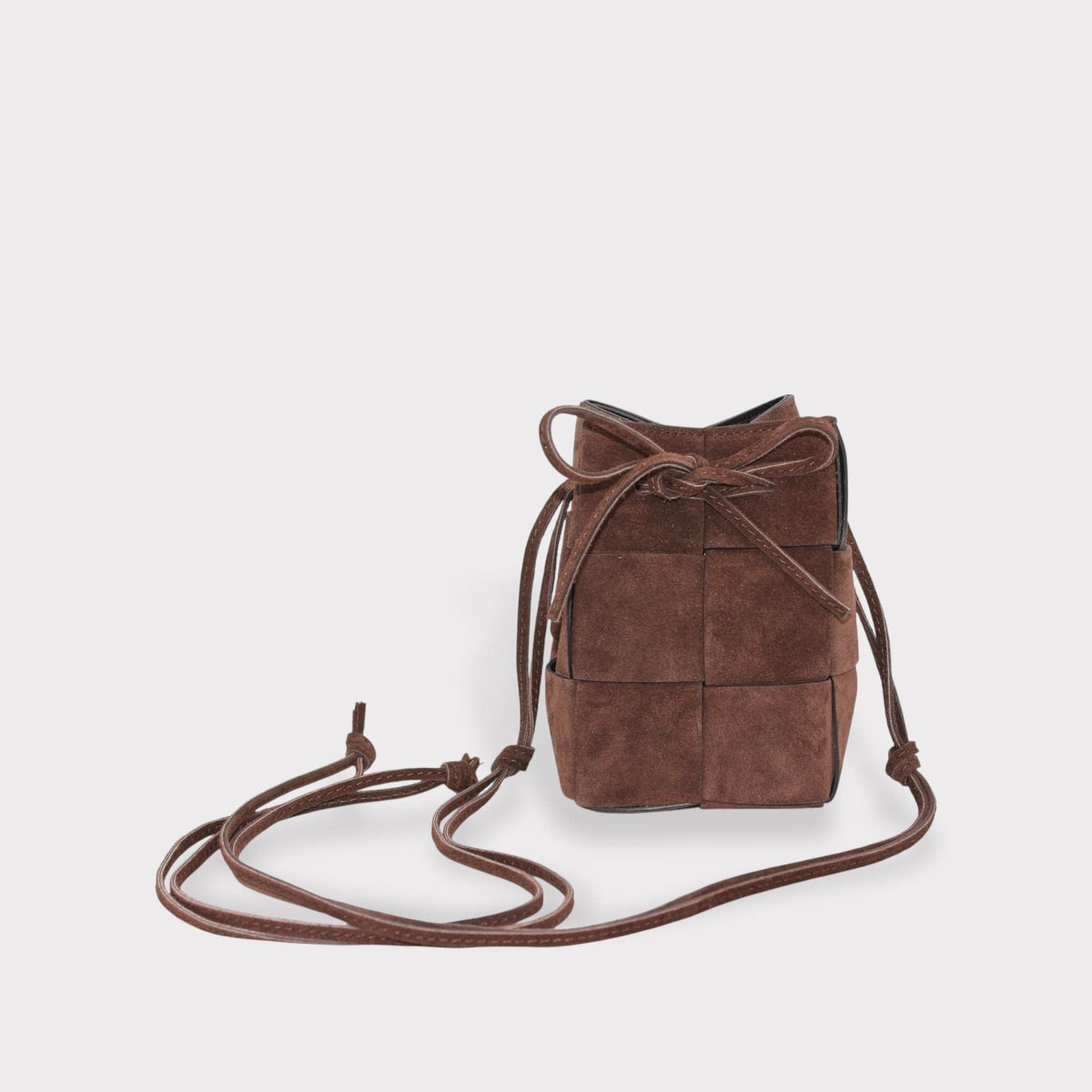 brown suede leather bucket bag with woven panel design and drawstring closure on light gray background