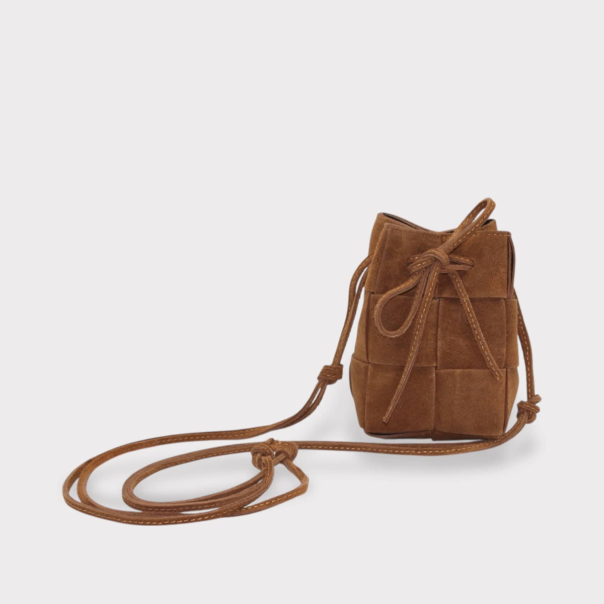 suede bucket bag in brown with woven texture and drawstring closure on light grey background