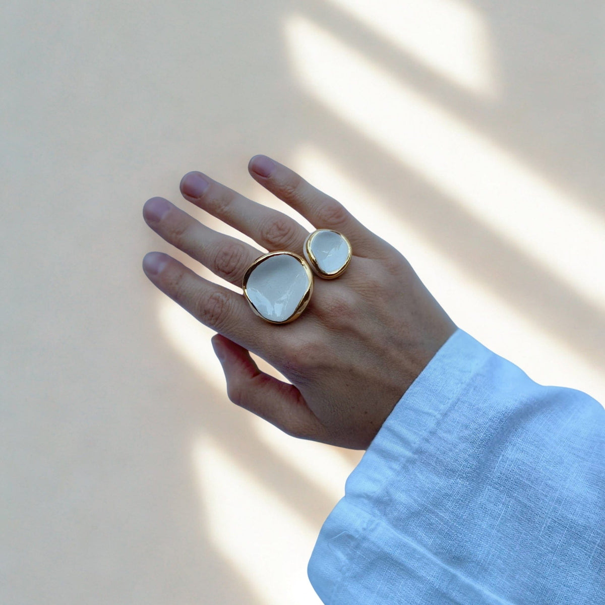 Hand mit zwei weißen Keramikringen mit goldfarbenen Rändern am Mittel- und Ringfinger