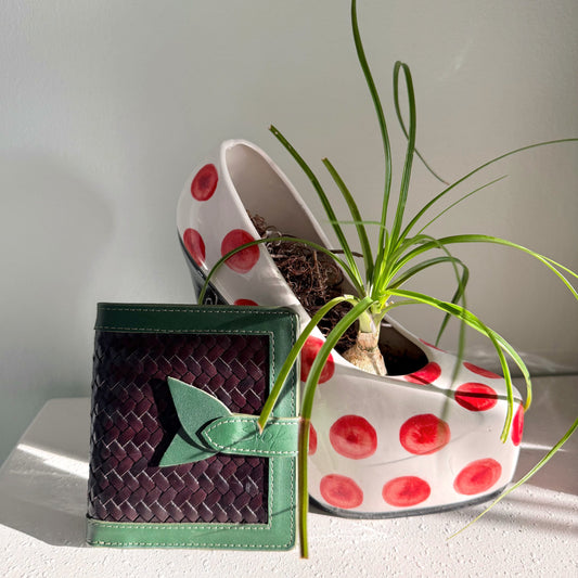Lumi - Handwoven Leather Wallet | Green&Dark Coffee with woven dark coffee leather and green leather trim beside a white pot with red dots and plant.