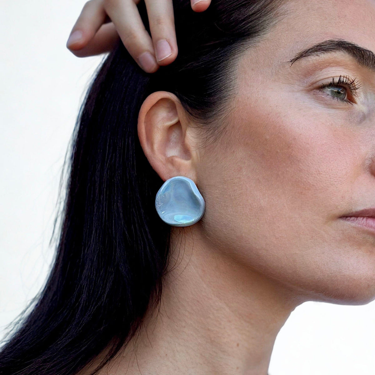 Perla light blue ceramic stud earring worn on the ear by a model
