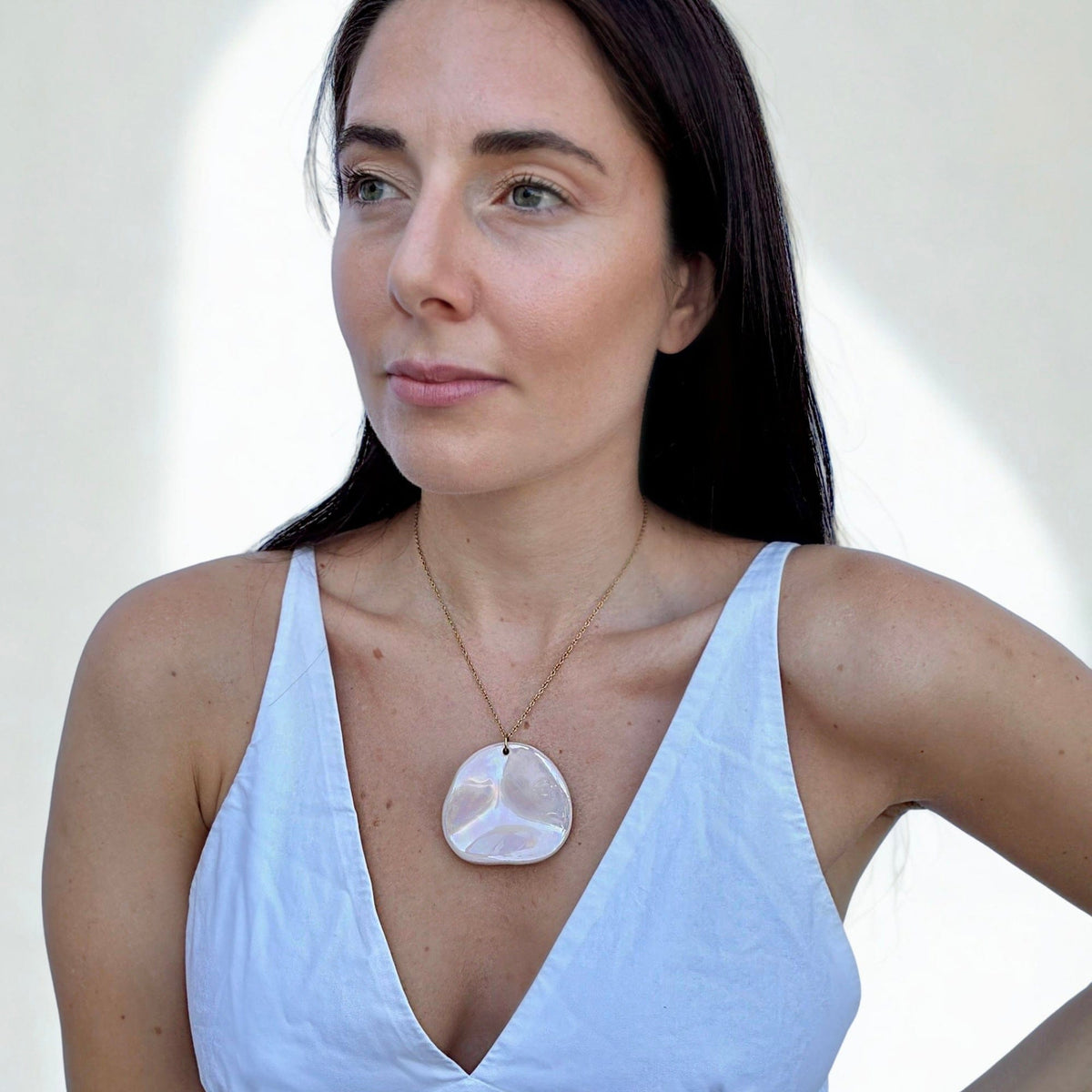 Model wearing pearl-pink ceramic pendant necklace on a gold chain over a light blue V-neck top