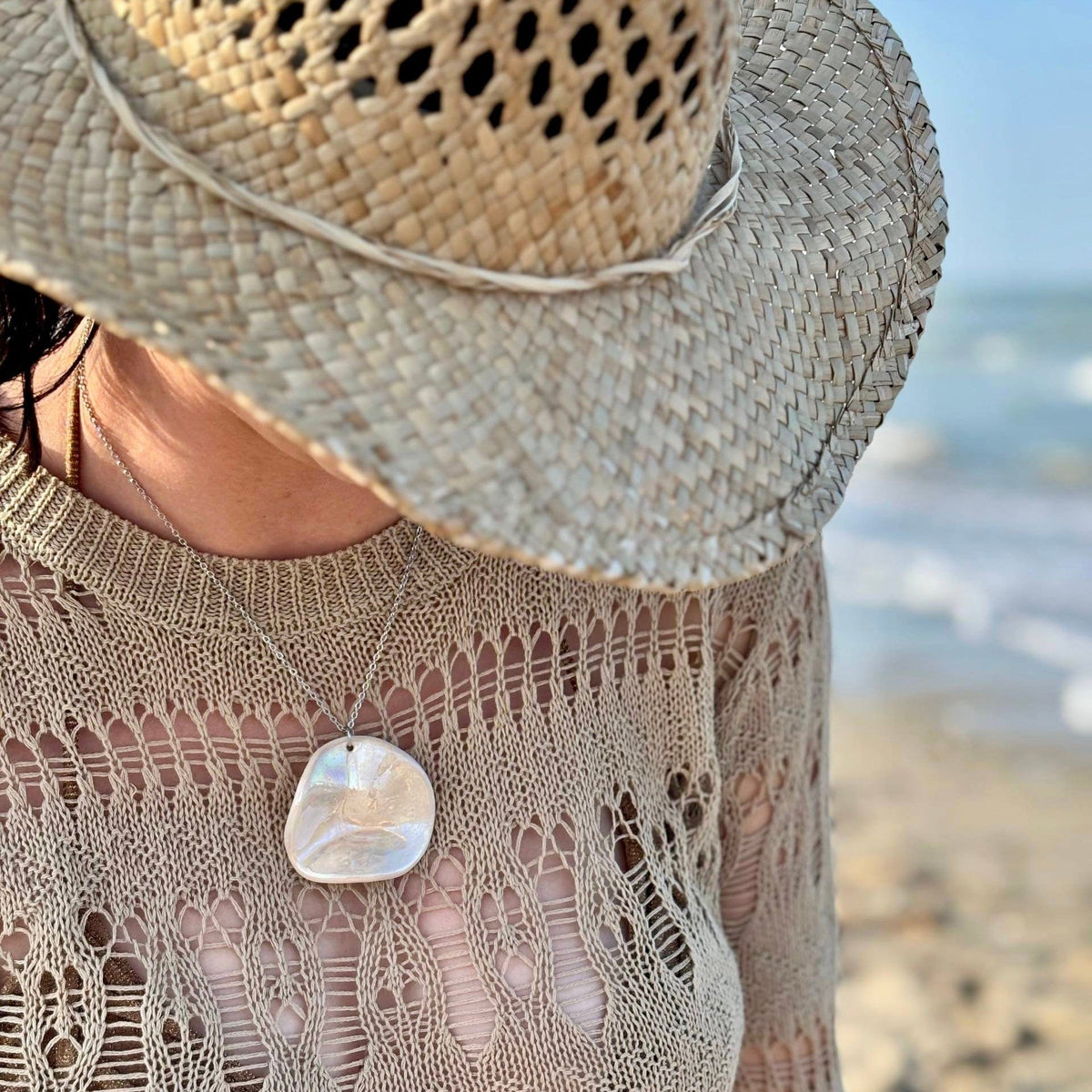 Woman wearing the pearl-white ceramic pendant necklace at the beach with a wide straw hat.