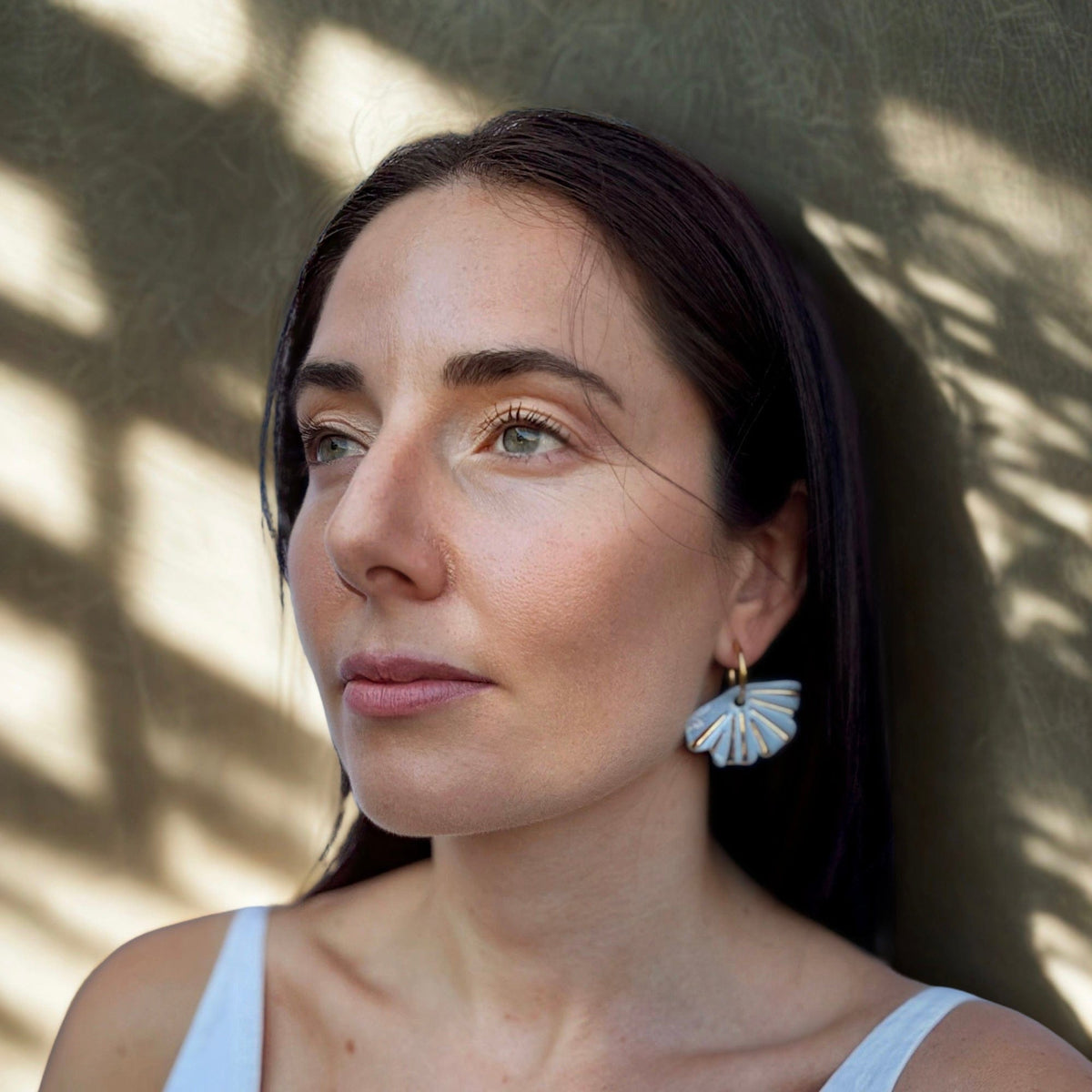 Selene handcrafted light blue ceramic dangle earrings with golden details worn by a woman