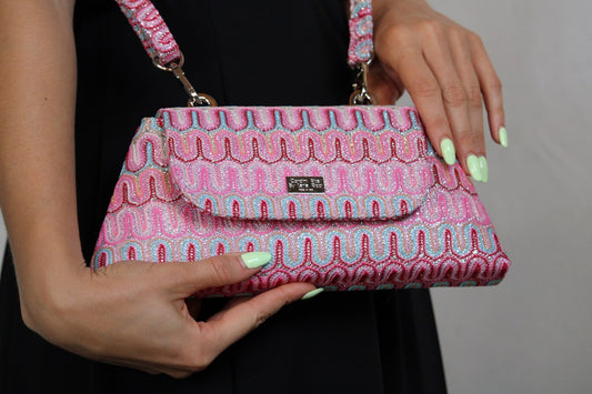 Mala rosa estampada com design ondulado, segurada por uma pessoa com unhas verde-menta.