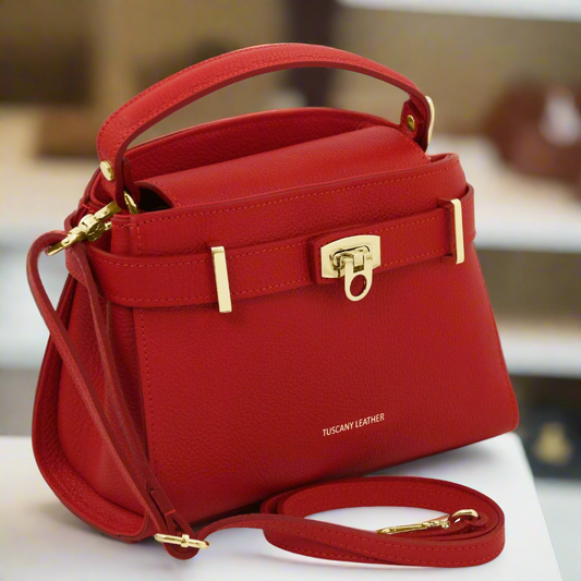 Close-up of a red leather handbag with gold hardware and a detachable strap on a white surface