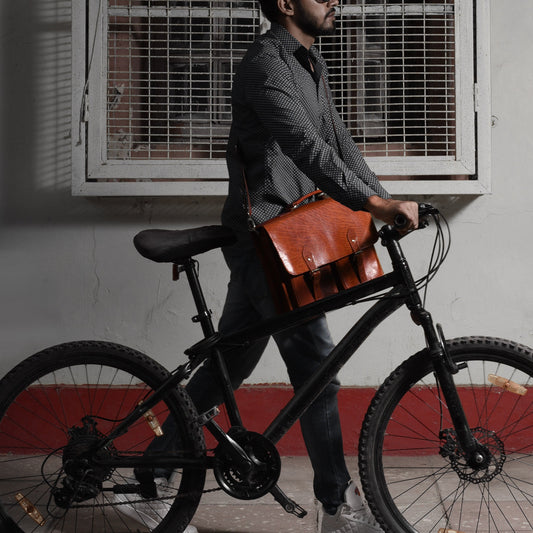 Man standing beside a black bicycle with a brown leather messenger bag slung across the frame.