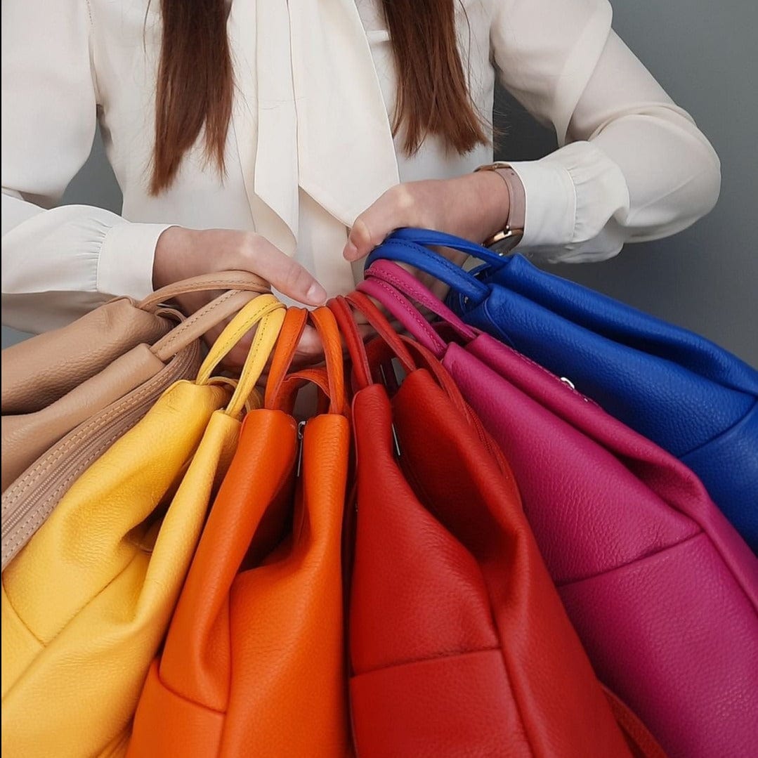 Person in a white blouse displays a fan of colorful leather handbags in rainbow hues.