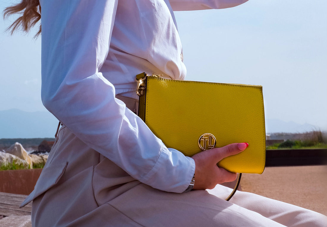 Primer plano de un bolso de piel amarillo intenso sostenido por una persona al aire libre.