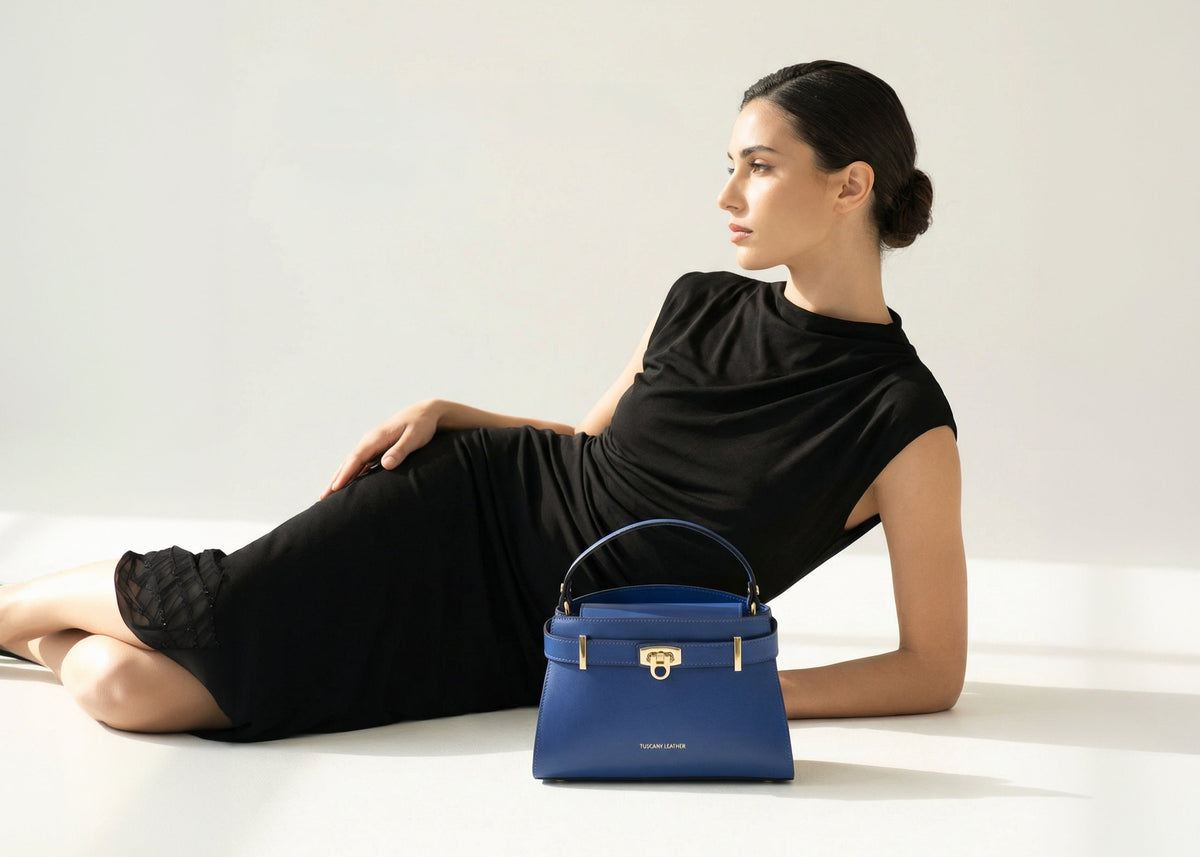 Blaue Handtasche mit goldfarbenen Metallteilen neben einer liegenden Frau in schwarzem Kleid.