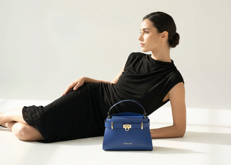 Blue handbag with gold hardware resting beside a reclining woman in a black dress.