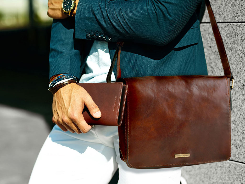 Mano che tiene un portafoglio marrone in pelle accanto a una borsa messenger coordinata.