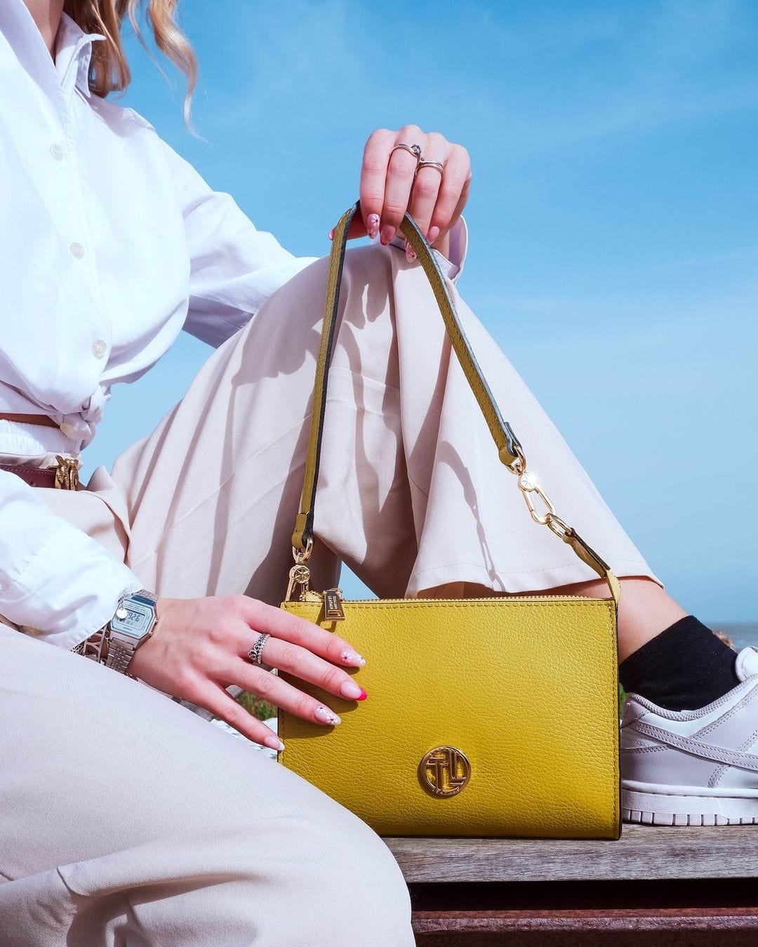 Clutch gialla brillante in pelle con manico superiore e accessori metallici dorati, tenuta da una persona con camicia bianca.
