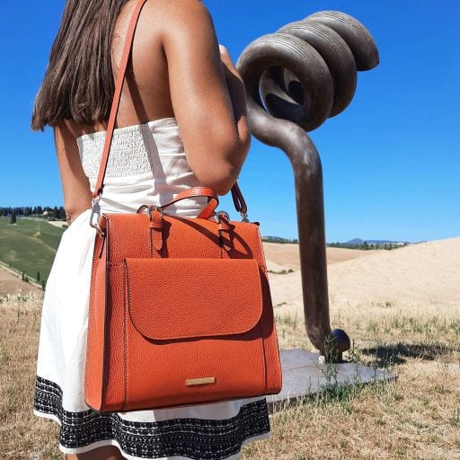 Orange convertible leather handbag with top flap and crossbody strap in an outdoor setting