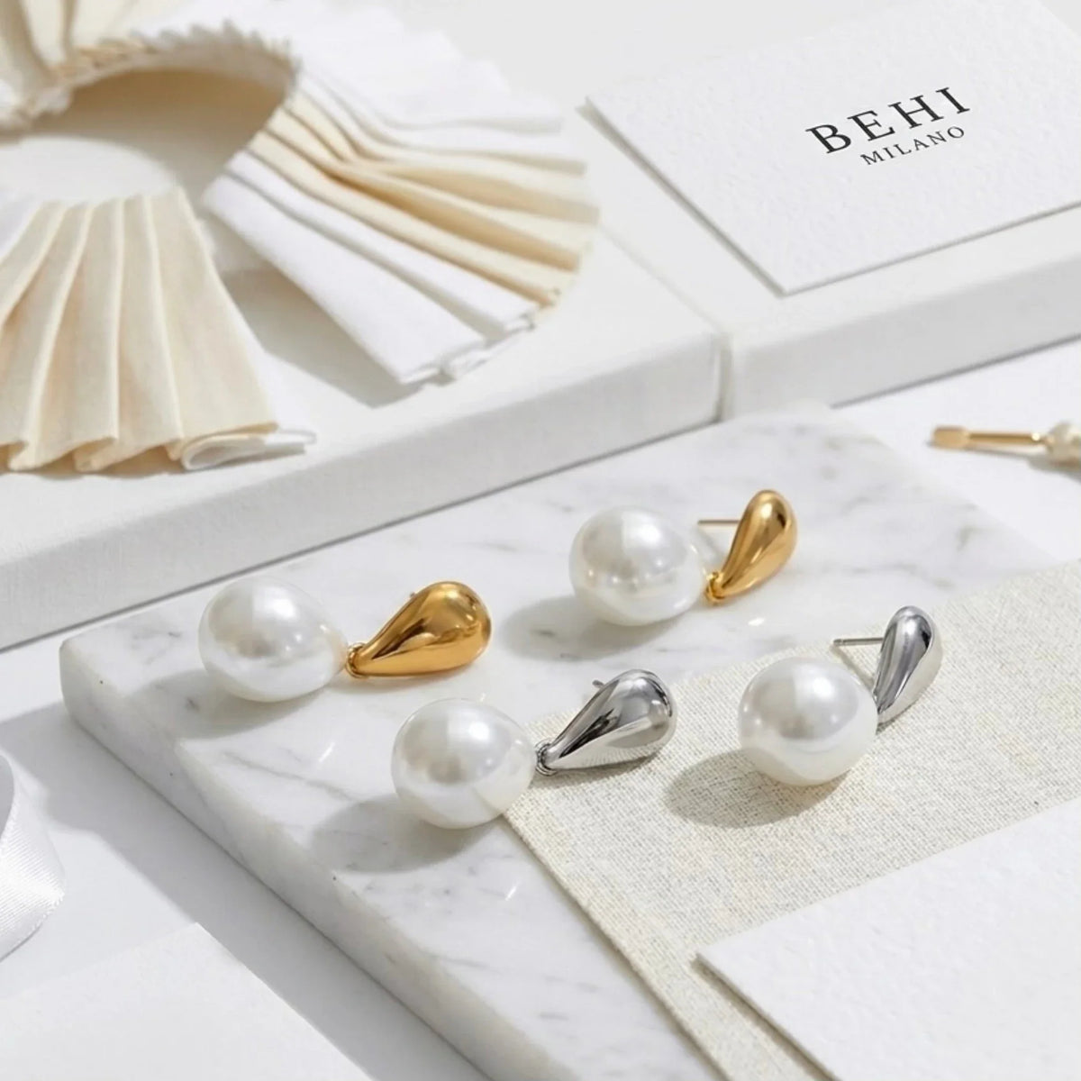 Boucles d’oreilles en perles aux tons doré et argenté sur une surface en marbre avec le marquage « BEHI MILANO »