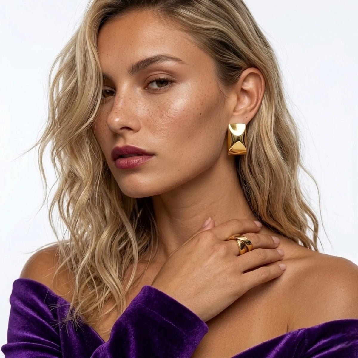 Donna con gold earrings e ring, con a purple top against a bianco background