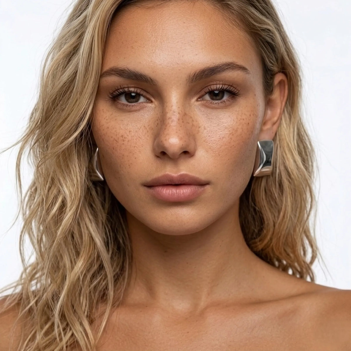 Primo piano of a woman con blonde hair e freckles wearing silver earrings su sfondo bianco