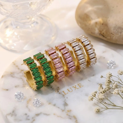 Set di orecchini dorati con gemme verdi, rosa e trasparenti su una superficie in marmo