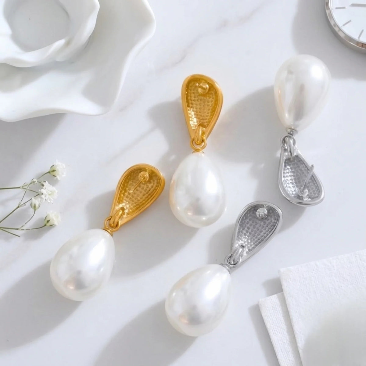 Dos de boucles d’oreilles en perles avec fermoirs dorés et argentés sur une surface blanche avec fleurs et horloge