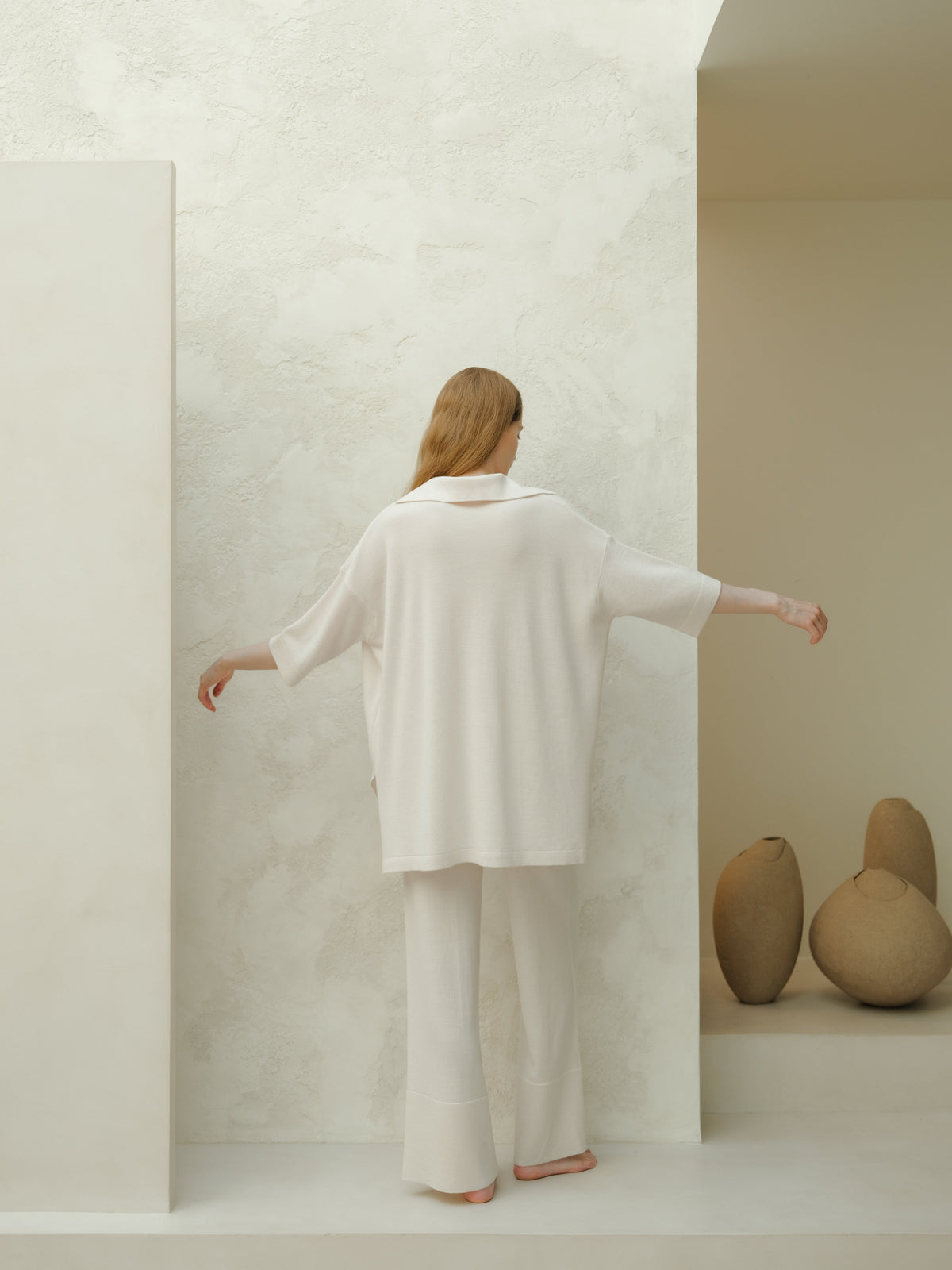Vue de dos d’un mannequin en maxi polo oversize blanc en laine mérinos devant un mur clair texturé