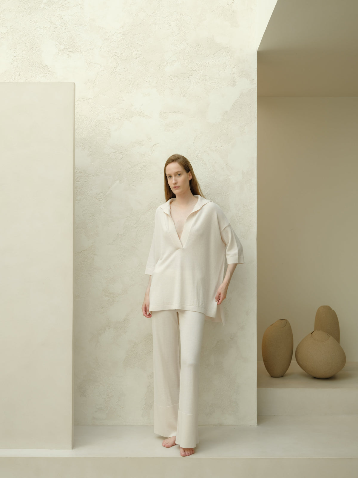 Full body view of a model in an off white Maxi polo en laine mérinos extrafine paired with matching wide leg pants in a minimalist studio.