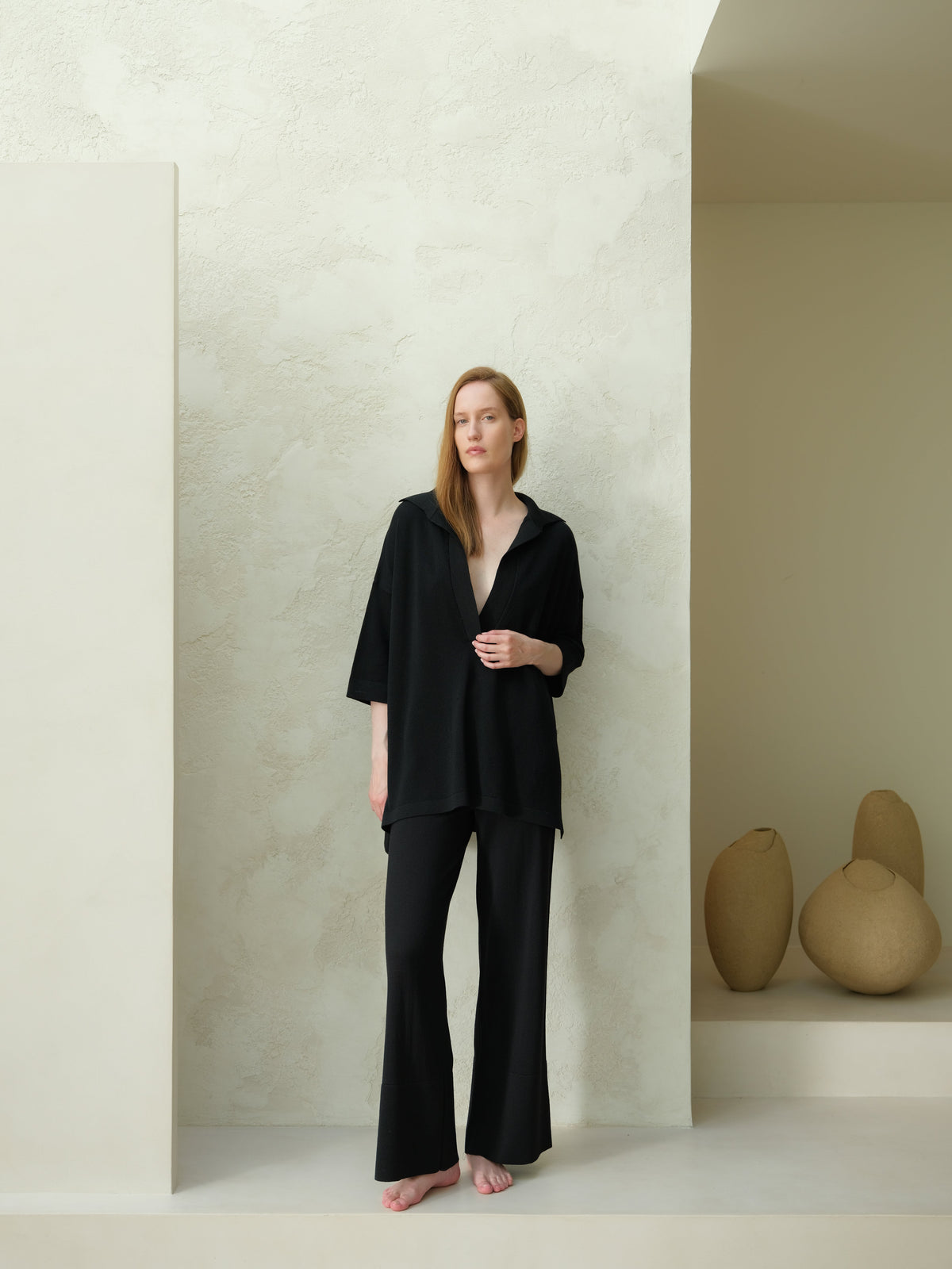 Full-body view of a model in a black Maxi polo en laine mérinos extrafine paired with pantalon large in a minimalist studio.