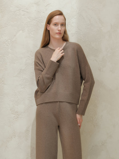 Modella con taupe cashmere mix maglione girocollo con matching trousers davanti a una parete chiara testurizzata