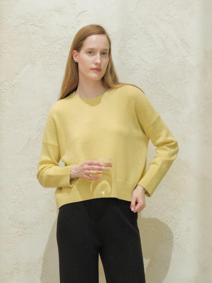 Modella con pale yellow cashmere mix maglione girocollo con nero pants davanti a una parete testurizzata.