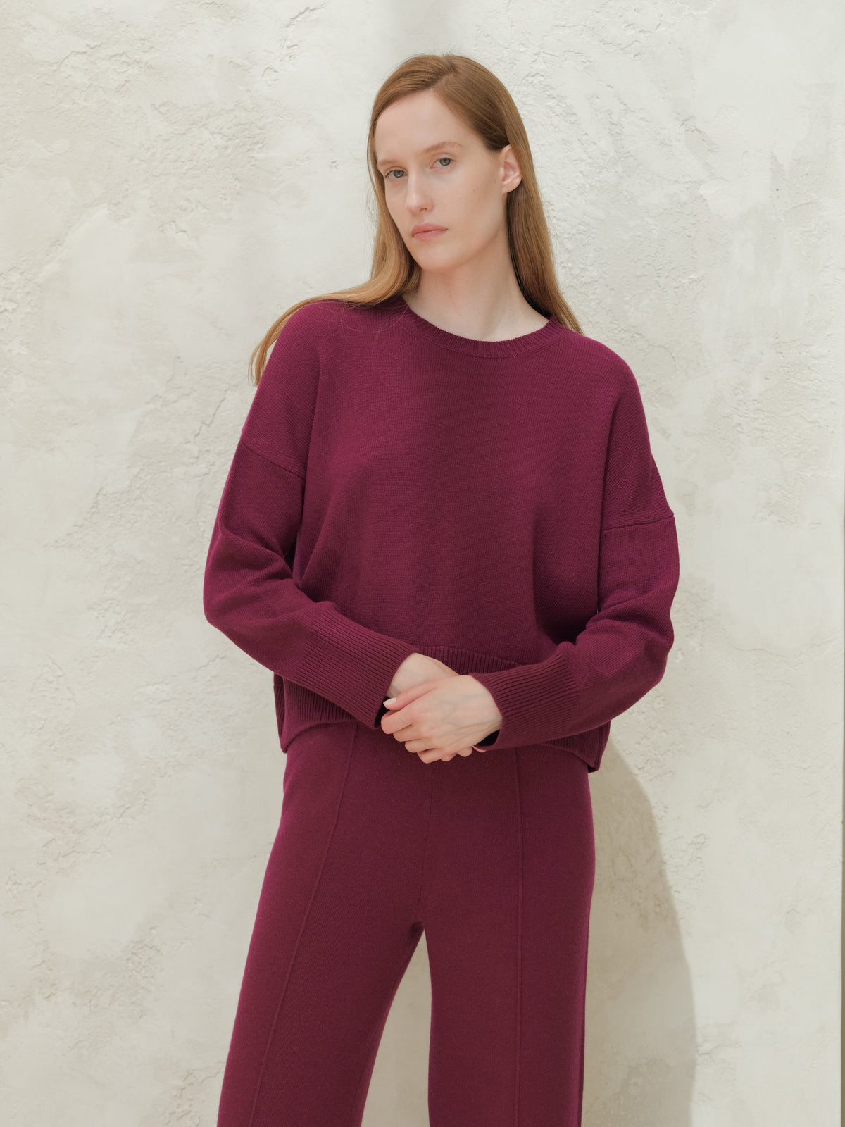 Modella con a deep bordeaux cashmere mix maglione girocollo con matching knit pants against a texturosso light wall