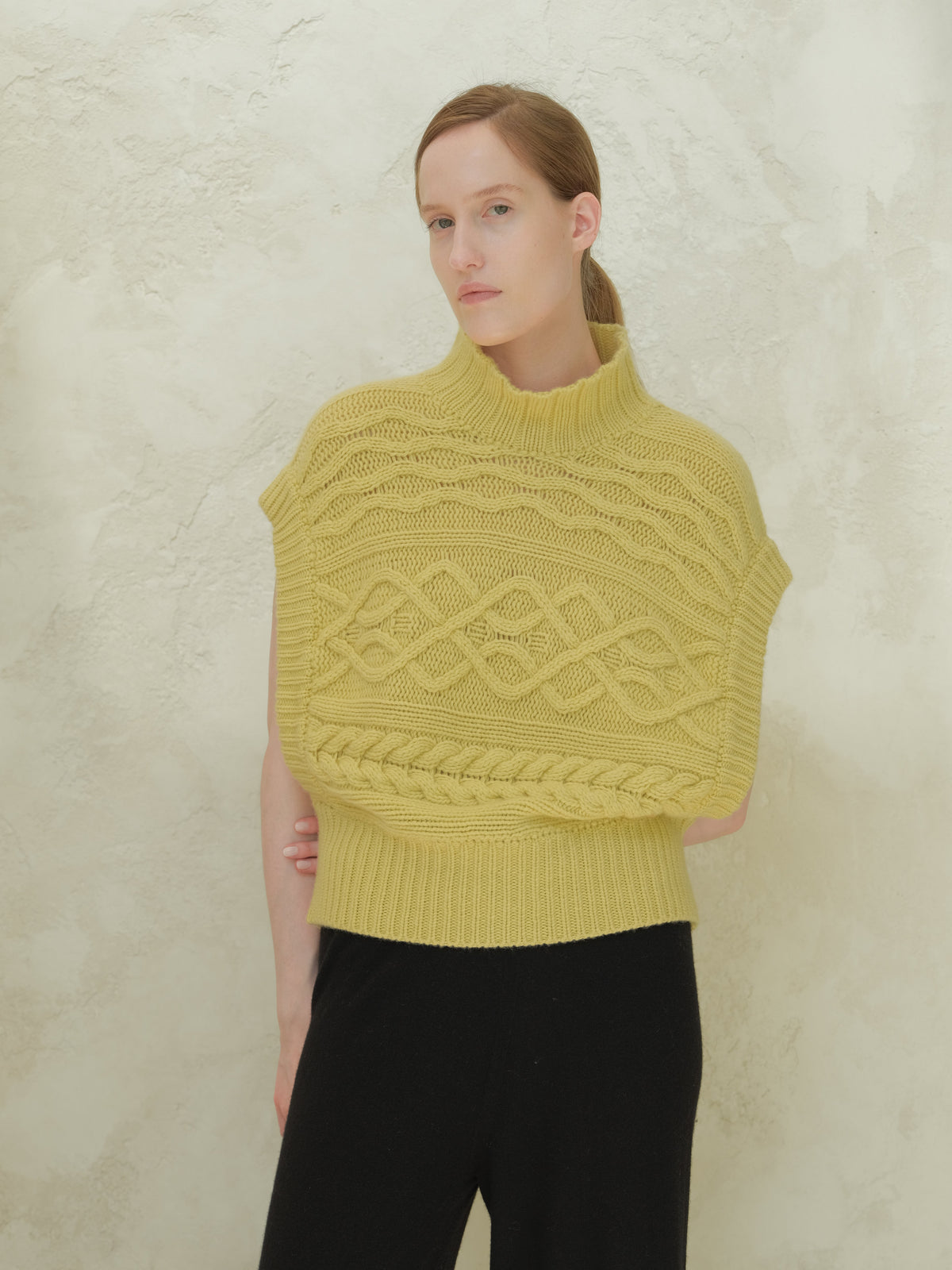 Front view of a modella con a yellow cashmere mix maxi tunica a trecce con a high ribbed collar e bold cable patterns.
