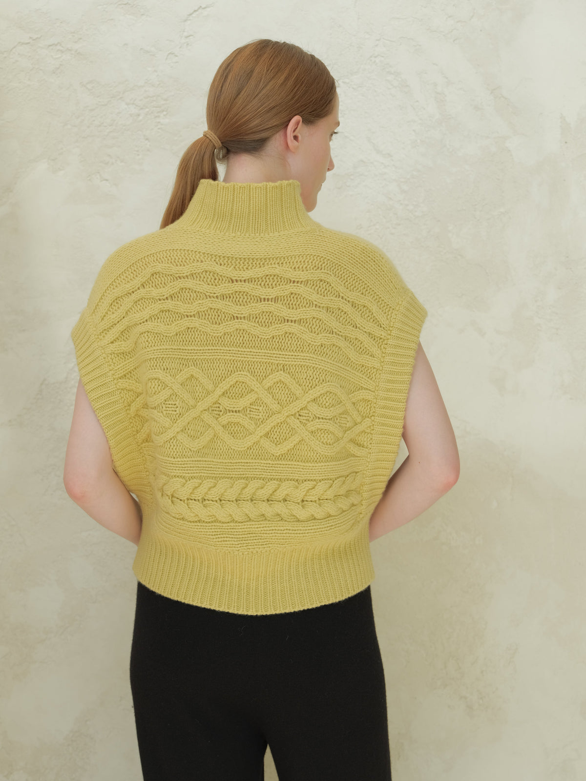 Back view of a pale yellow cable knit maxi tunic con collo alto e intricate patterns.