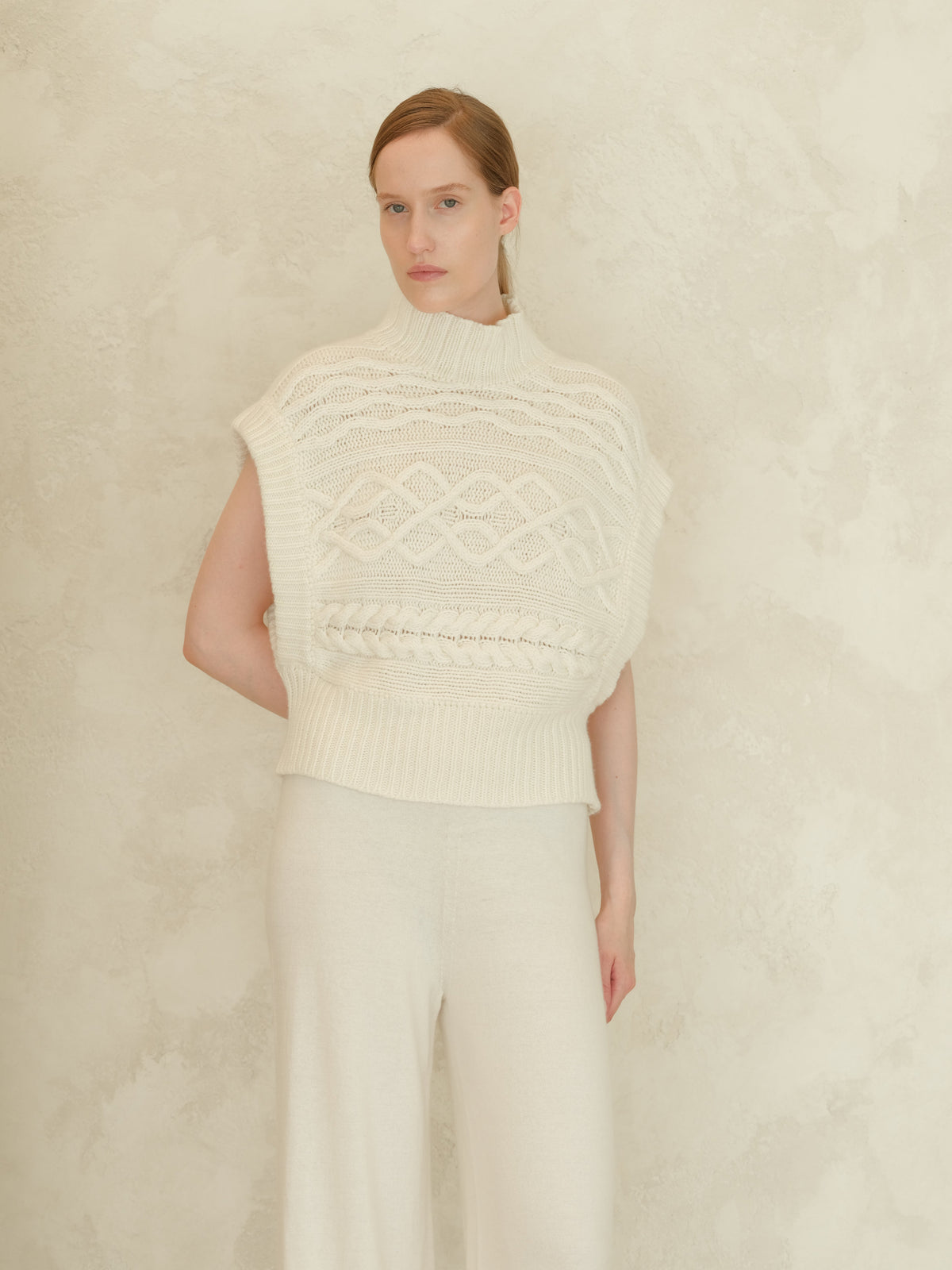 Crema Maxi tunica a trecce in misto cashmere worn by a model con a high ribbed neck e chunky knit cable pattern.
