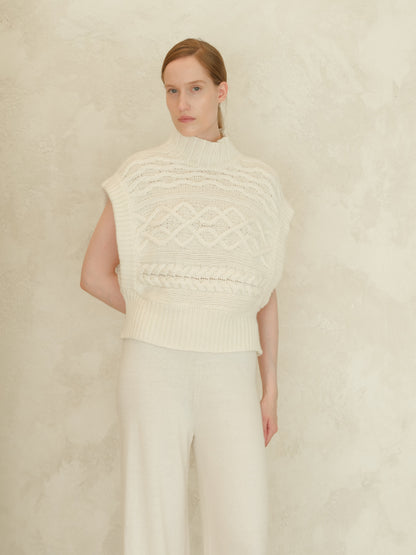 Crema Maxi tunica a trecce in misto cashmere worn by a model con a high ribbed neck e chunky knit cable pattern.