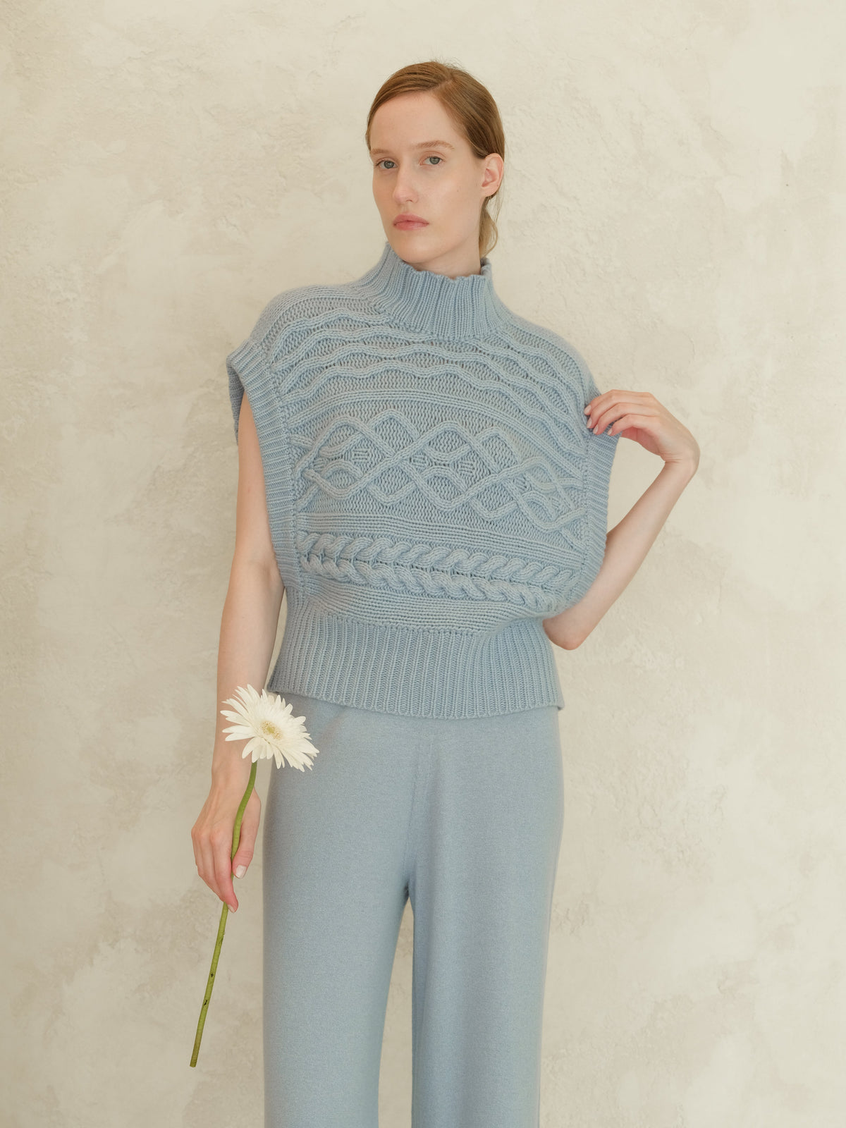 Modella con blu cashmere mix maxi tunica a trecce con a high ribbed neck e sleeveless silhouette davanti a una parete testurizzata.