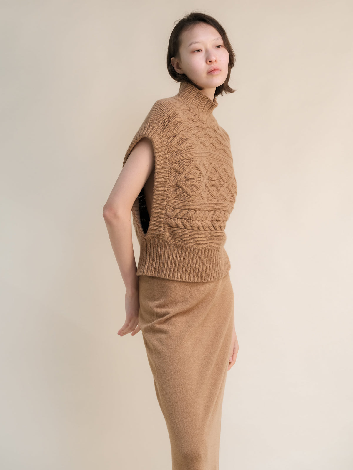 Profile view of a modella con a cuoio cashmere mix maxi tunica a trecce con a high ribbed neck e bold knit patterns.