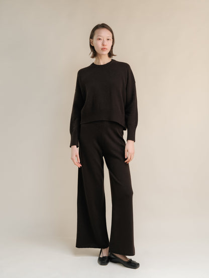 Full-length shot of a model in a dark marrone cashmere mix maglione girocollo con pantaloni coordinati a gamba larga.