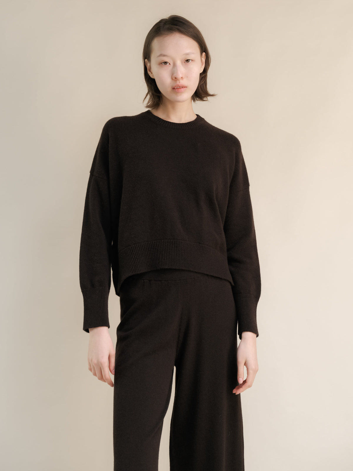 Modella con a dark marrone cashmere mix maglione girocollo con pantaloni coordinati a gamba larga.