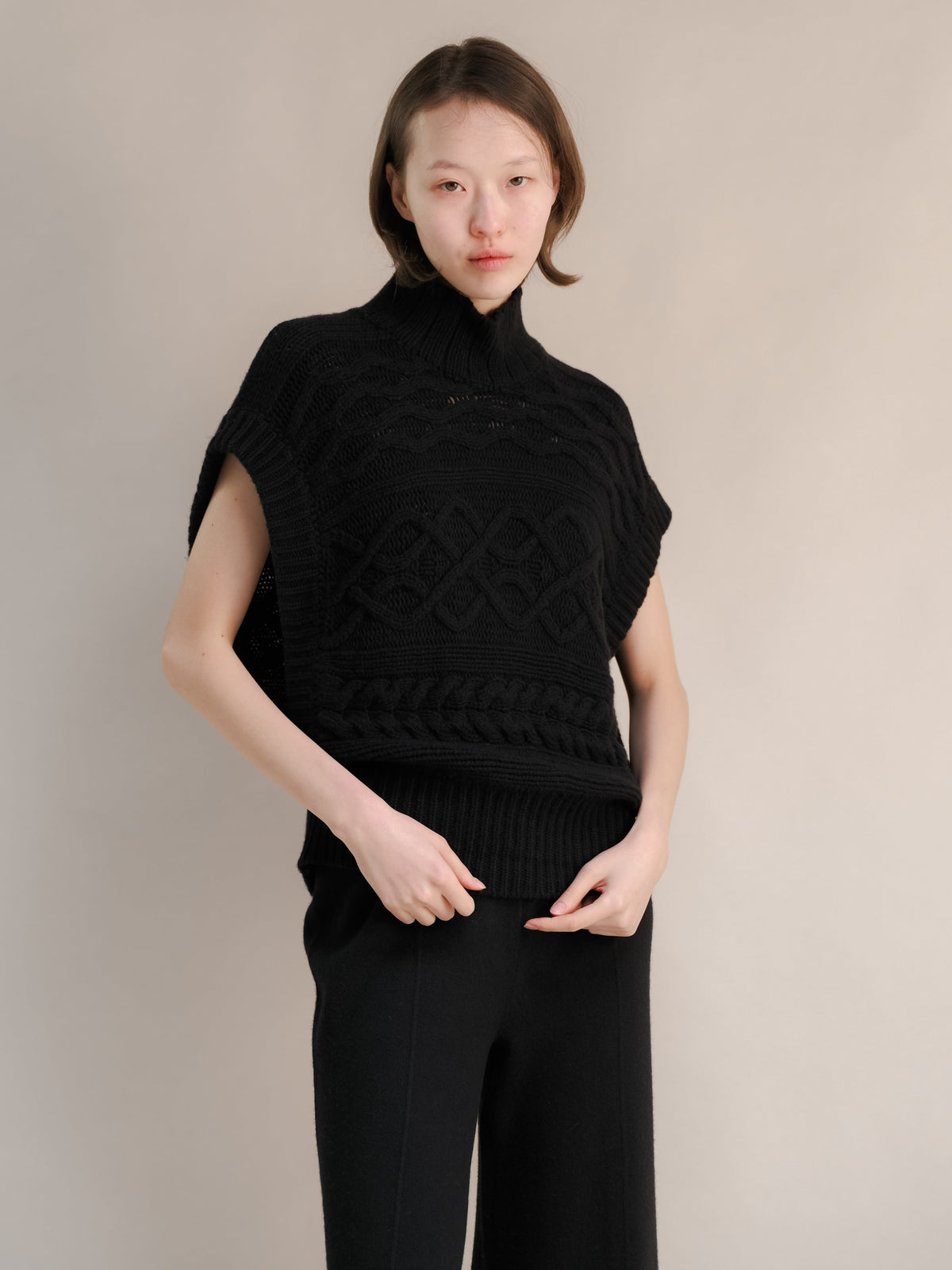 Modella con a nero cashmere mix maxi tunica a trecce con a snug collo alto e chunky cable patterns.