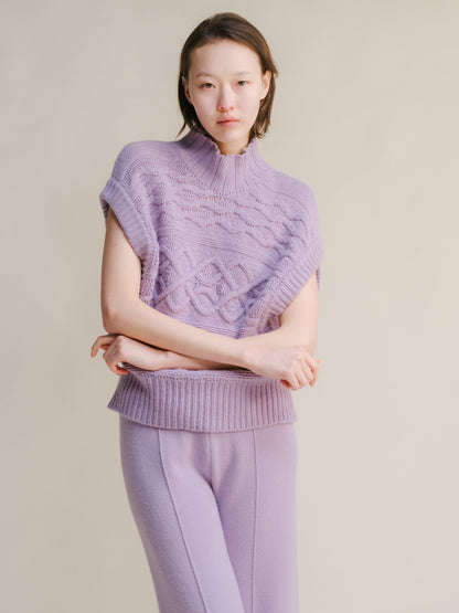 Lilla chunky knit sleeveless tunic con a collo alto e cable pattern worn con matching lilac pants.