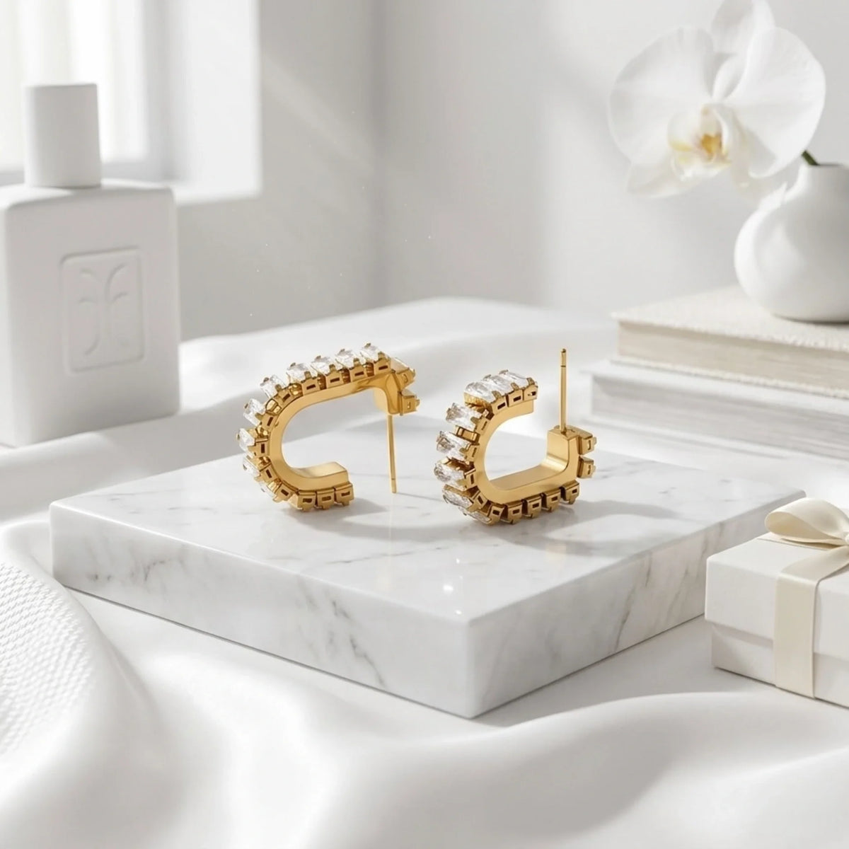 Orecchini a cerchio dorati su una superficie in marmo con orchidea bianca e confezione regalo sullo sfondo