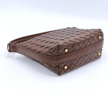 Genuine leather woven boxed pouch bag in brown with gold studs at its base, shown from the side.