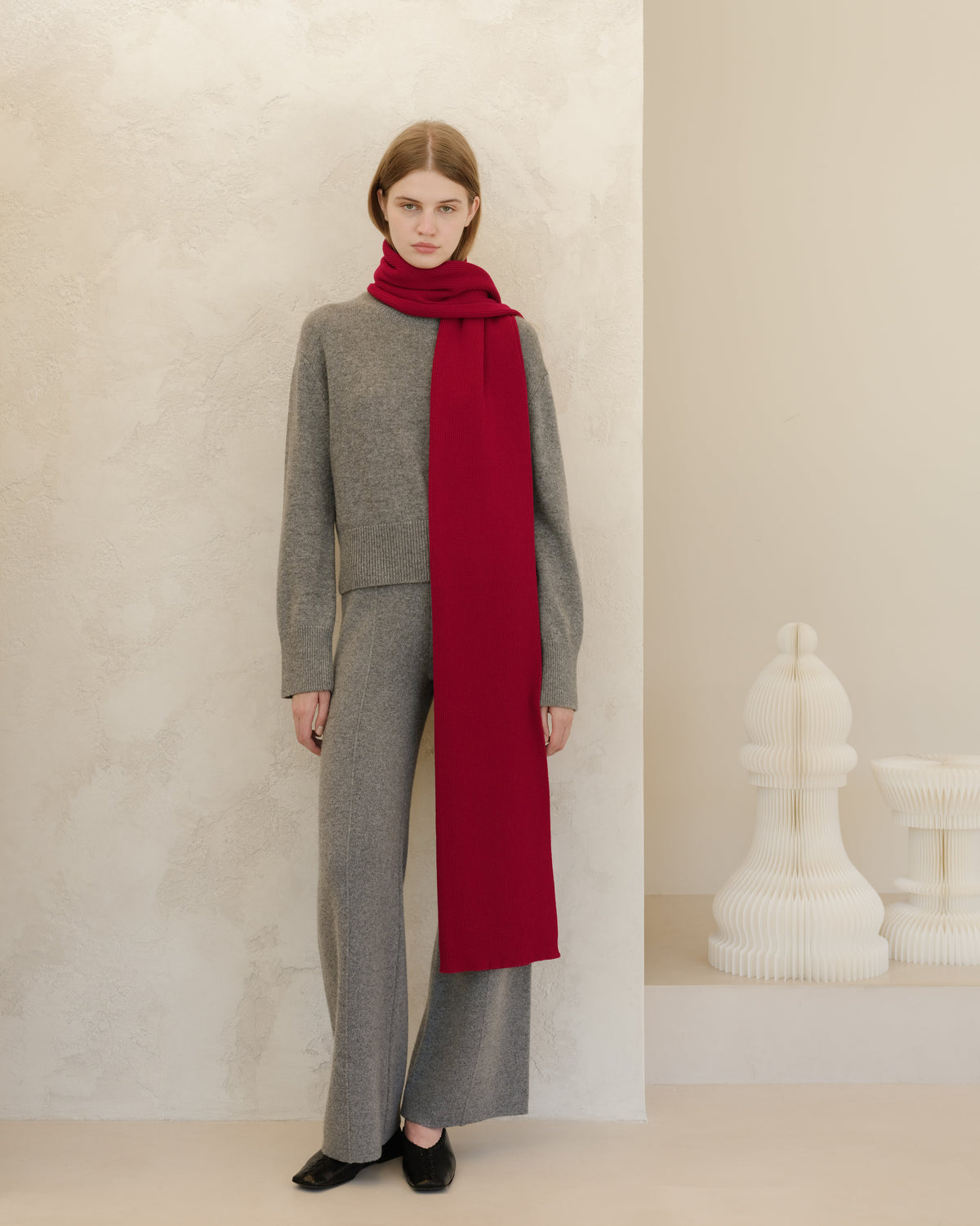 Person in grauem Outfit mit langem rotem Schal vor neutralem Hintergrund