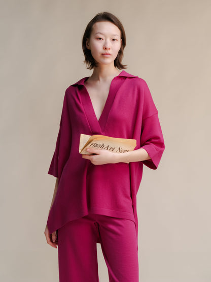 Rose vif merino wool maxi polo worn by a model with a deep V neckline, holding a folded newspaper