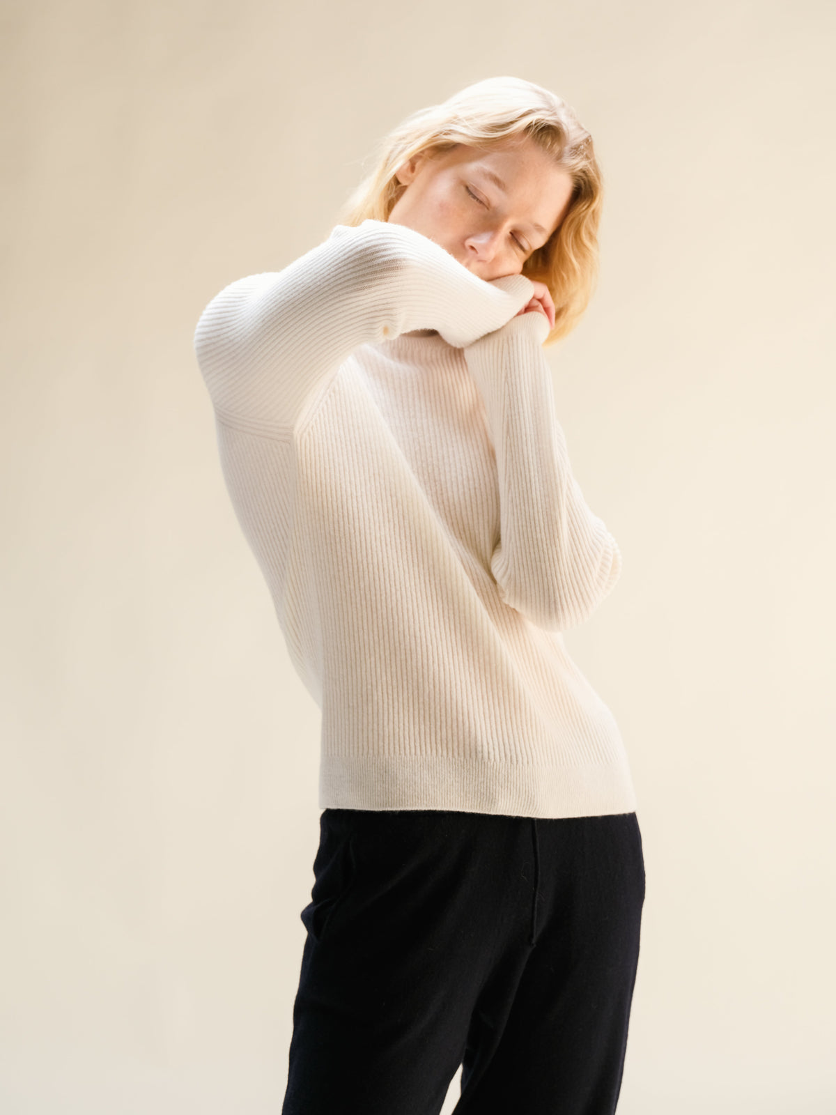 Donna con bianco ribbed cashmere mix mock neck sweater, vista posteriore con arms raised.