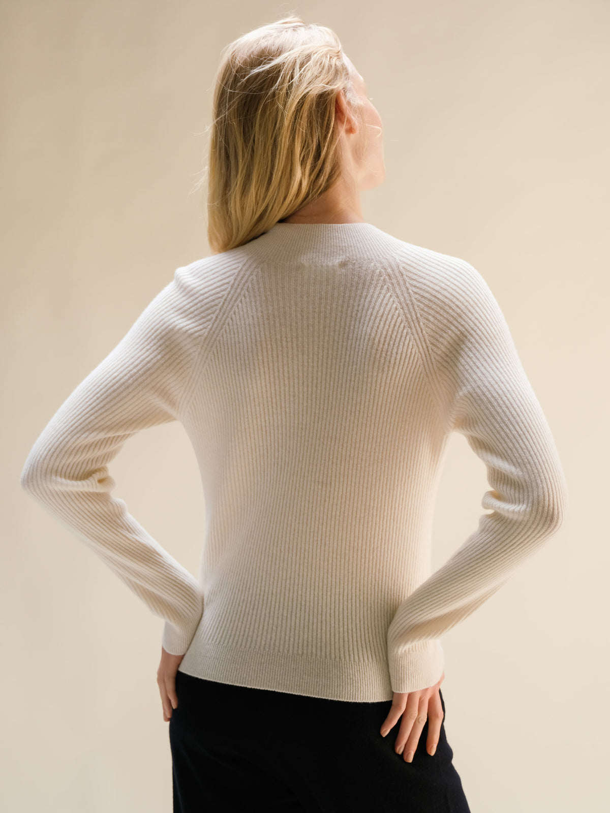 Modella con crema ribbed cashmere mix mock neck sweater, vista posteriore con hes on hips.