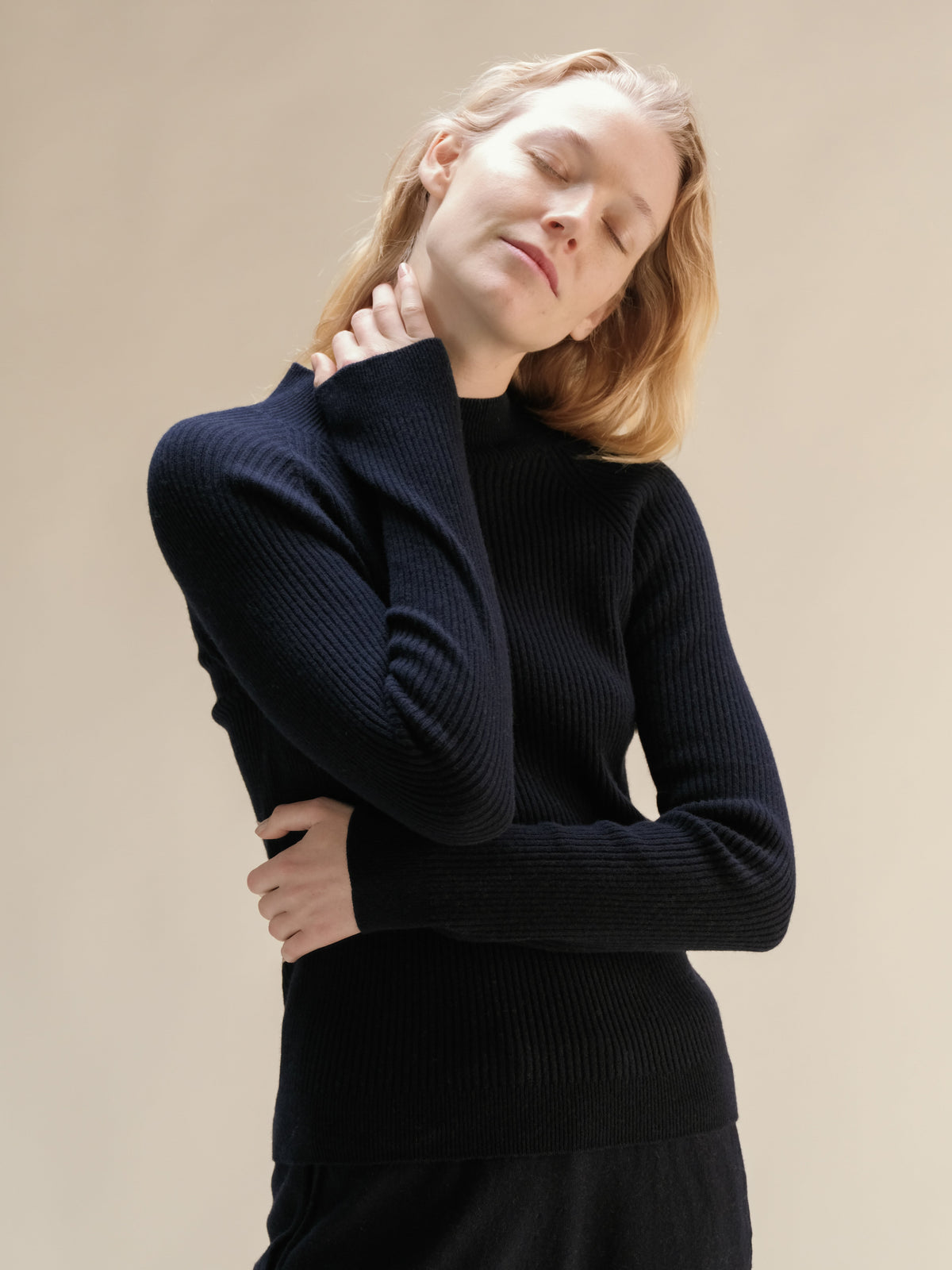 Modella con navy cashmere mix maglione a coste con collo alto posing con eyes closed highlighting the soft knit.