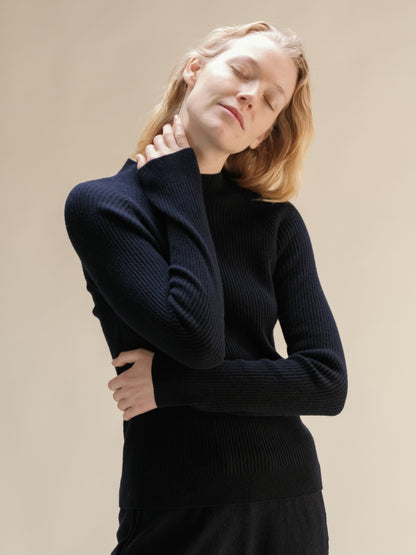 Modella con navy cashmere mix maglione a coste con collo alto posing con eyes closed highlighting the soft knit.