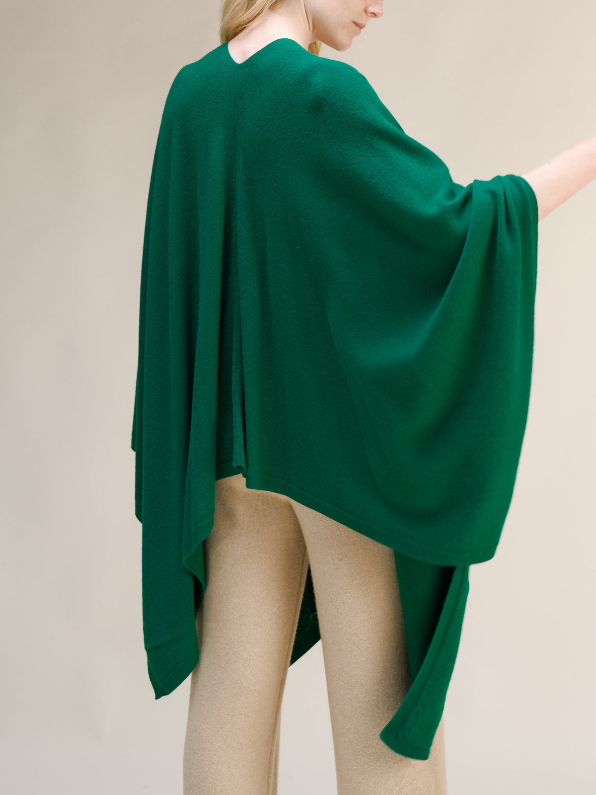 Verde cashmere mix maxi cape draped over a model from the back, con beige pants visible.